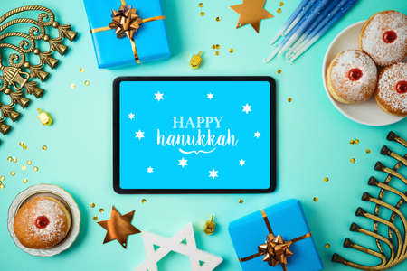 Jewish holiday Hanukkah concept with digital tablet mock up, menorah, sufganiyah and gift box over blue backgroundの写真素材