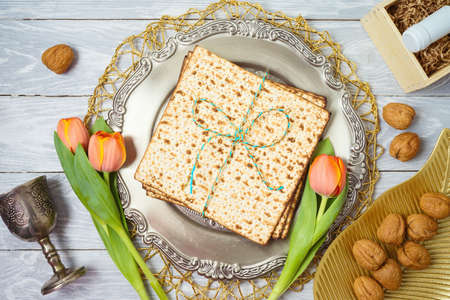 Jewish holiday Passover background with matzah, seder plate, wine and tulip flowers on wooden tableの写真素材