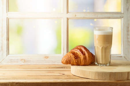 Coffee cup and croissant on wooden table over window backgroundの写真素材