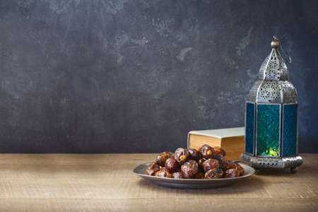 Lightened lantern and dates fruit on wooden table over dark background. Ramadan kareem holiday...