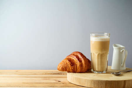 Coffee cup and croissant on wooden table over gray backgroundの写真素材