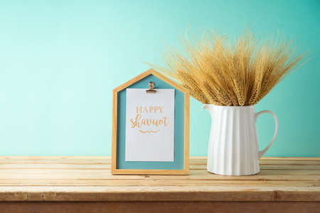 Wheat in vase and photo frame on wooden table over blue wall background. Shavuot holiday mock up for design.の写真素材