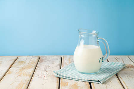 Milk jug on wooden table with tablecloth over blue background. Kitchen mock up for designの写真素材