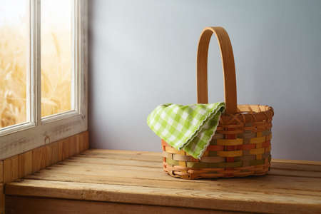 Empty basket with tablecloth on wooden table over window and wall background. Harvest and Shavuot mock up for design.の写真素材