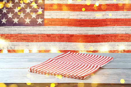 Empty wooden table with striped tablecloth over American flag background. 4th of july USA...