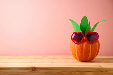 Halloween pumpkin creative decor as pineapple with sunglasses on wooden tableの写真素材