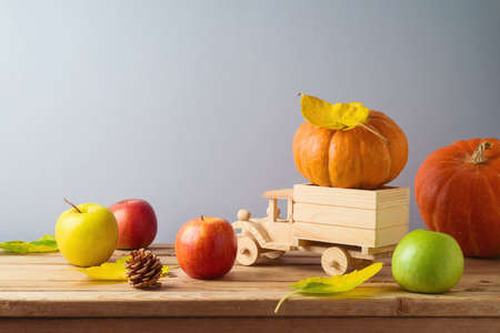 Thanksgiving holiday and autumn season concept with pumpkin, apples and fall leaves in toy truck on wooden tableの写真素材