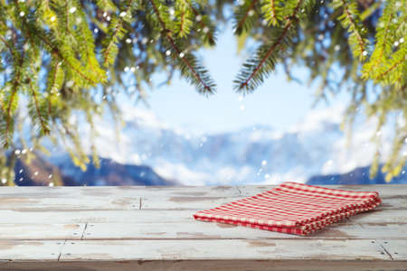 Empty wooden table with red checked tablecloth over winter landscape background.  Christmas and New Year mock up for design and product display.の写真素材