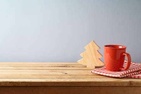 Wooden table with coffee cup and wooden Christmas tree over gray wall background.  Christmas and New...