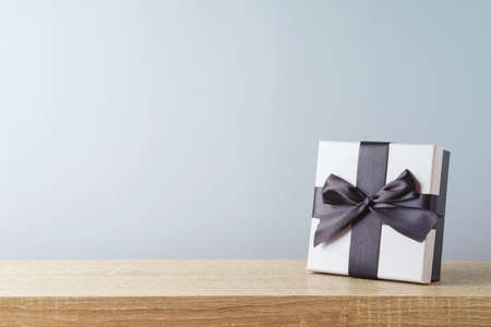 Gift box with black bow on wooden table. Sale concept mock up for design and product display.の写真素材