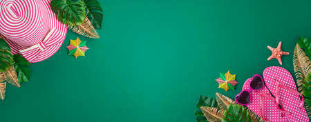 Summer holiday vacation concept with beach accessories and tropical leaves on green background. Top...