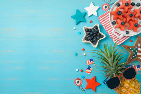 USA Independence Day concept. Summer fruit salad, pineapple and decorations on blue background. Top...