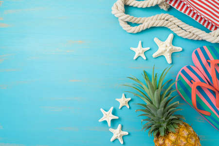 Summer beach vacation background. Pineapple, flip flips and beach bag on wooden board. Top view, flat layの写真素材