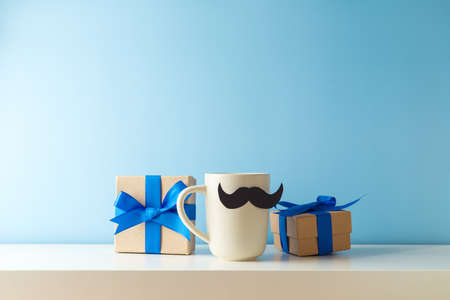 Happy Father's day celebration with coffee cup, mustache and gift box on white table over blue backgroundの写真素材