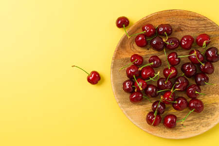 Summer food concept. Red cherries in wooden plate over yellow backgroundの写真素材