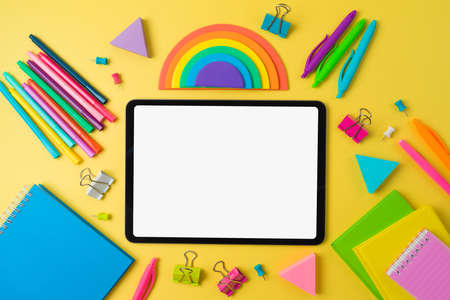 Back to school concept with digital tablet, notebooks and rainbow sticky notes on yellow background....