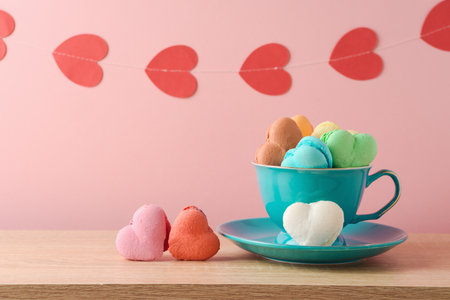 Heart shape macaroons french cookies in coffee cup with heart shape garland over pink background. Valentines day greeting cardの写真素材