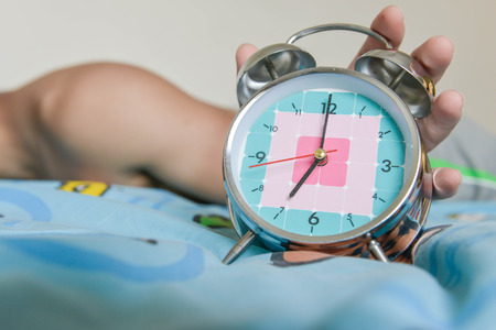 sleepy man is expanding hand to stop the alarm clock that showing time for 7 AM