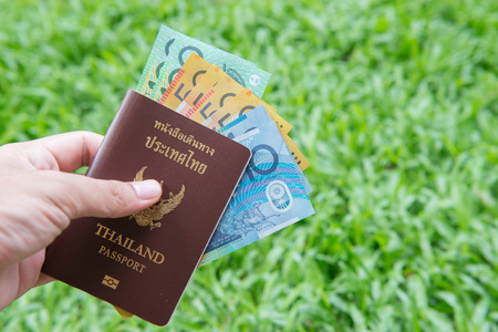 Hand hold Thailand passport and australian money with green grass backgroundの写真素材