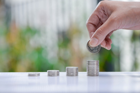 Woman hand putting coin to growing coins stacks - Concept of saving money