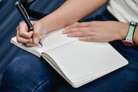 Business woman is writing note to notebook with pen