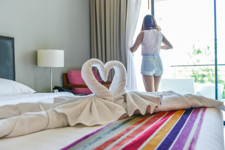 Towel design as swans on the bed in the hotel and background with women is opening curtainの写真素材