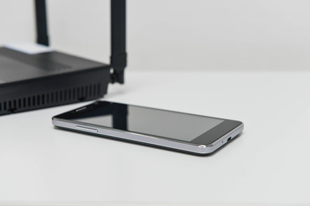 Black mobile phone connected to the wireless router on the white tableの写真素材