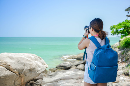 Backpacking women is taking the photo with digital camera on the seashoreの写真素材