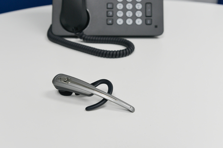 Wireless headset is on the white table with black IP or office phone at behind