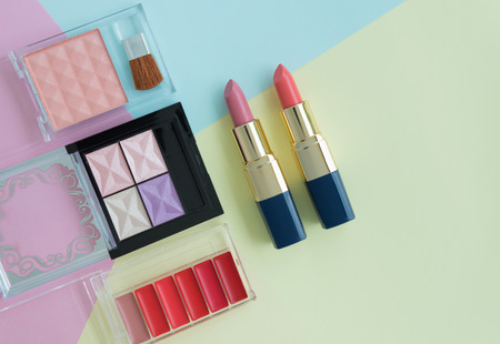 Flat lay creative concept of female decorative cosmetic for orange and pink lipstick, lipstick palette and eyeshadow palette on the colorful background with copy spaceの写真素材