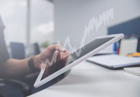 Business man is holding the tablet, double exposure of candlestick chart for finance and trading