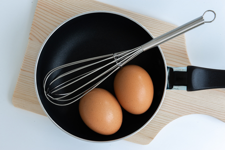 Close up pan with egg and stainless steel egg whisk and chopping on the white backgroundの写真素材