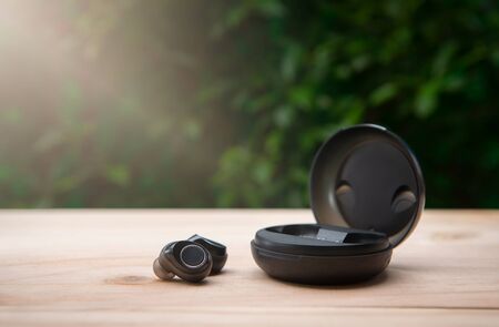 Black true wireless earbuds with power bank case on the wooden table with green background