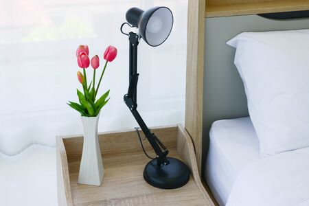 Close up of modern bed and bedside cabinet with flower vase in the bedroomの写真素材