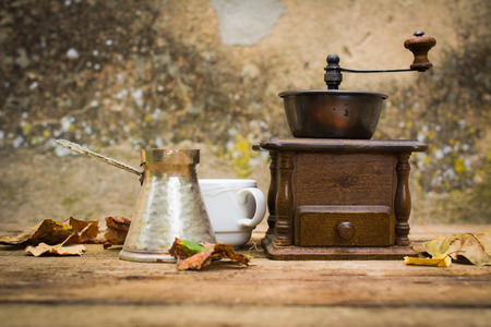 Old coffee grinder on a wooden table surrounded by autumn leaves.の写真素材