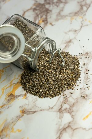 selective focus, small Chia seeds scattered from a glass jar. They have very useful properties, are used as an additive in salads and dessertsの写真素材