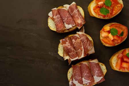 selective focus, snack bruschetta, with red tomatoes and Basil, and smoked meats. On a small white bread baguette on a dark backgroundの写真素材