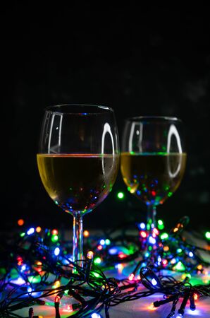 Transparent wine glasses in the light of Christmas colored bulbs. With highlights, in a low key, on a dark backgroundの写真素材
