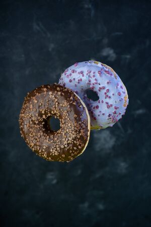 selective focus, flour product. levitating sweet doughnuts with chocolate and blueberry icing, with chocolate and fruit topping. On dark backgroundの写真素材