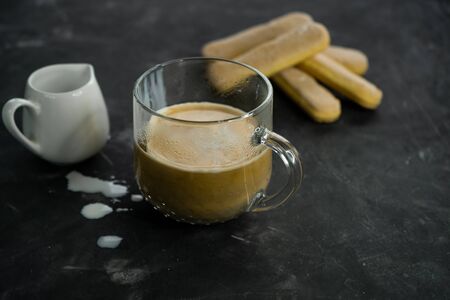 a mug of hot black coffee beans with cream and air biscuits savoyardi. On dark backgroundの写真素材