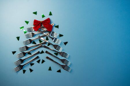 selective focus, an alternative Christmas tree of table forks on a blue background, with Christmas powder and a bowの写真素材
