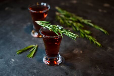 cherry, berry and spicy tincture of alcohol and berries in the glasses. on a dark background, with a sprig of rosemary. Minimalism, low keyの写真素材