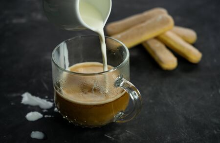 a mug of hot black coffee beans with cream and air biscuits savoyardi. On dark backgroundの写真素材