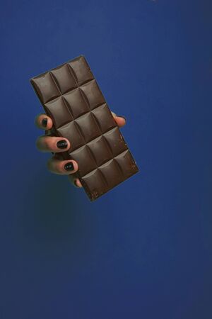 selective focus, a female hand in a round hole, in the background, holding a dark chocolate barの写真素材