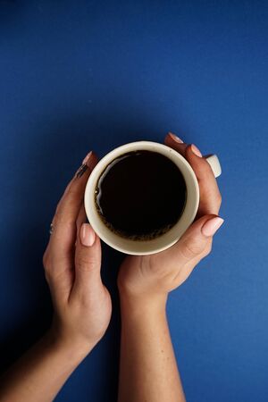 selective focus, female hands holding a mug of black tea on a blue backgroundの写真素材