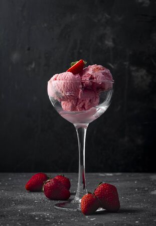 strawberry ice cream balls with strawberry berries, in a high transparent glass on a dark backgroundの写真素材