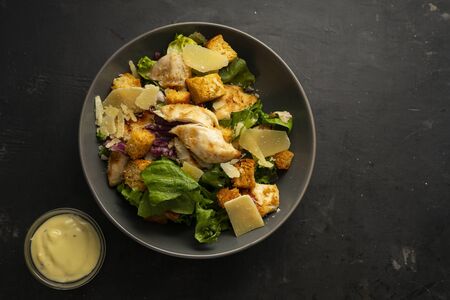 selective focus, Italian Caesar salad with chicken, Parmesan and crackers, in a dark frosted plate on a dark tableの写真素材
