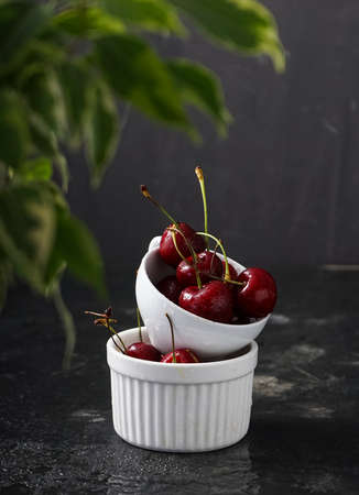 Selective focus, ripe cherries with water drops in a ceramic white Cup, on a dark background,...