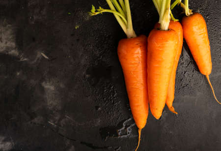 Selective focus, ripe fresh carrots with a green stem on a black table, copyspaceの写真素材