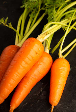 Selective focus, ripe fresh carrots with a green stem on a black table, vertical positionの写真素材